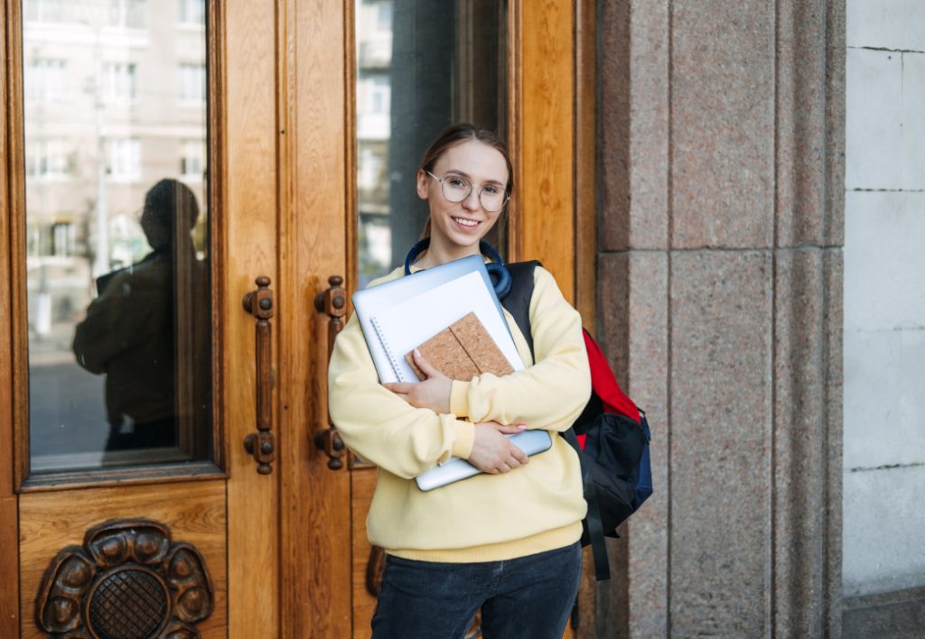 Female college student standing in front of university with books